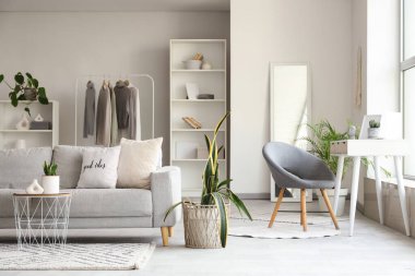 Gri kanepeli, kahve masalı, ev bitkisi ve işyeriyle aydınlık oturma odasının içinde.