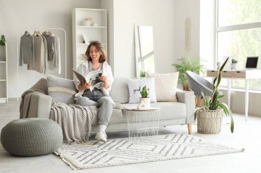 Genç, güzel bir kadın, oturma odasındaki kanepede dergi okuyor.