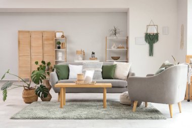 Gri kanepeli, sehpalı, koltuklu ve raflı aydınlık oturma odasının içi.