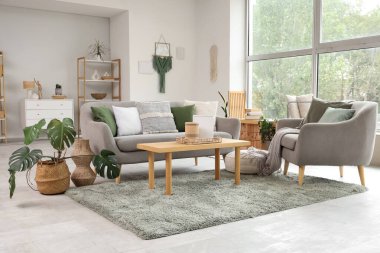 Gri kanepeli, kahve masalı, koltuklu ve pencereli aydınlık oturma odasının içi.