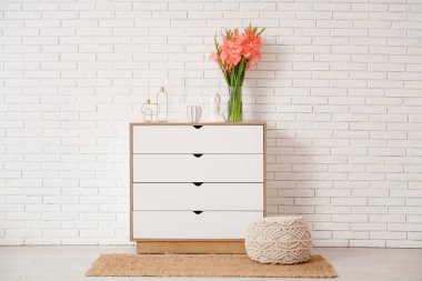 Gladiolus çiçekli vazo, Moai heykeli ve odasındaki beyaz tuğla duvarın yanındaki klozette mumlar.