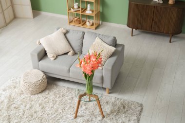 Oturma odasında, kanepe, puf ve gladiolus çiçekleri masanın üzerinde.