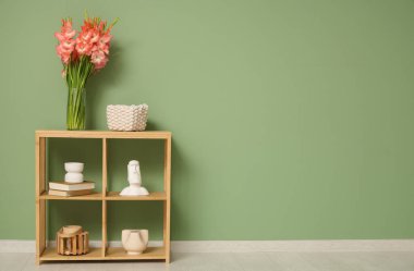 Odadaki yeşil duvarın yanındaki rafta gladiolus çiçekli vazo.