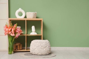 Oturma odasının içinde raf ünitesi, puf ve gladiolus çiçekleri vazoda.