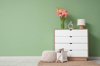 İçinde gladiolus çiçekleri, lamba ve biblo olan vazo yeşil duvarın yanındaki klozette.