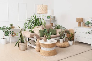 Kanepe, masa ve yeşil bitkilerle aydınlık oturma odasının içinde.