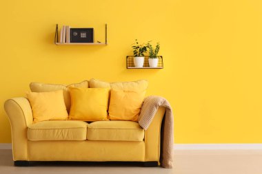 Kitaplı raflar ve oturma odasındaki sarı duvarda asılı modern kasalar.