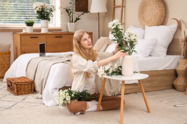 Güzel, genç, mutlu bir kadın vazoya bir buket beyaz kasımpatı koyuyor.