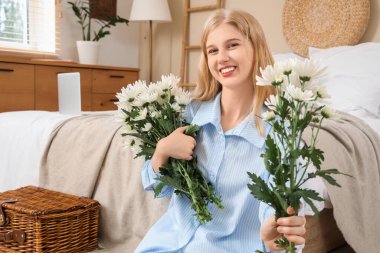 Evinde oturan güzel, mutlu, beyaz kasımpatı buketleriyle genç bir kadın.