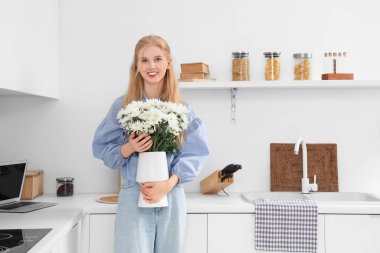 Evinin mutfağında bir buket beyaz kasımpatı çiçeğiyle güzel, genç ve mutlu bir kadın.