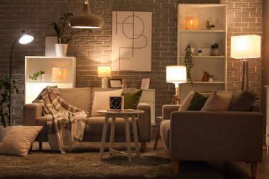 Sıcak kanepeler, sehpa ve oturma odasının içinde parlayan lambalar.