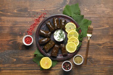 Lezzetli Dolmas tabağı (doldurulmuş üzüm yaprakları), ekşi krema, limon dilimleri ve ahşap arka planda baharatlar