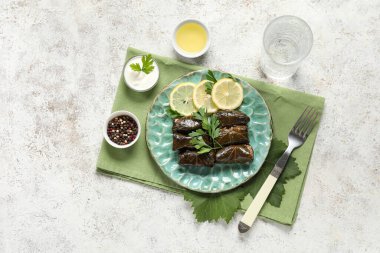 Lezzetli Dolmas tabağı (doldurulmuş üzüm yaprakları), ekşi krema, biber ve açık arkaplanda bir bardak su