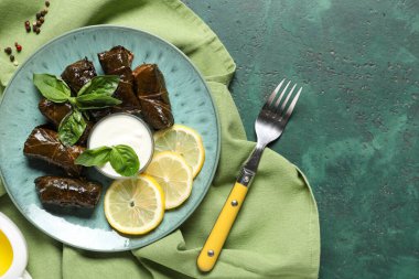 Lezzetli Dolmas tabağı (doldurulmuş üzüm yaprakları), limon dilimleri, ekşi krema ve çatalla renklendirilmiş arka plan