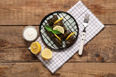 Lezzetli Dolmas tabağı (doldurulmuş üzüm yaprakları), ahşap zemin üzerinde limon ve ekşi krema