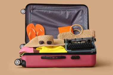 İçinde klasik daktilo ve bej arka planda plaj aksesuarları olan bavulu aç