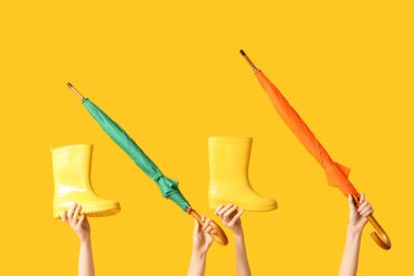 Şemsiyeli kadın elleri ve sarı arka planda çizmeleri.