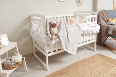 Çocuk odasının içindeki beyaz duvarın yanında ekose ve koltuklu şık bir beşik.