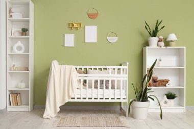 Çocuk odasının içindeki yeşil duvarın yanında ekose ve raf üniteli güzel bir beşik.