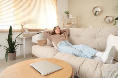 Oturma odasındaki bej koltukta uzanan genç kadın.