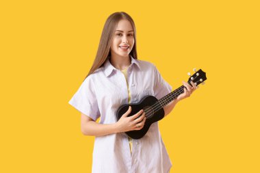 Sarı arka planda ukulele çalan genç kadın.