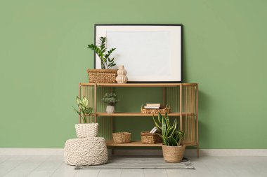 Raflar, ev bitkileri, pouf ve çerçeve yeşil duvarın yanında.