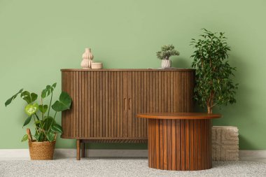 Çekmeceler, sehpa ve yeşil duvarın yanındaki bitkiler.