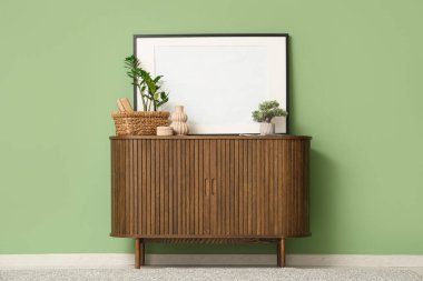 Sepet, vazo ve çerçeve yeşil duvarın yanındaki çekmecelerde.