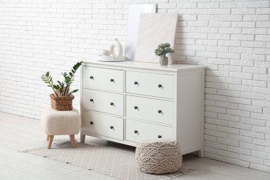 Çekmeceler, puflar, ev bitkileri ve odanın beyaz tuğla duvarının yanındaki çerçeveler.