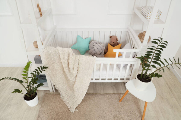 Interior of light children's bedroom with crib, toys and houseplants