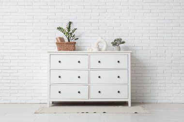 Beyaz duvarın yanındaki çekmecelerde dekorasyon ve bitkiler var.