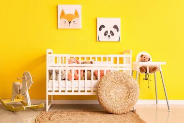 Bebek sandalyesi ve sarı duvarın yanında sallanan atı olan şirin oyuncaklar.