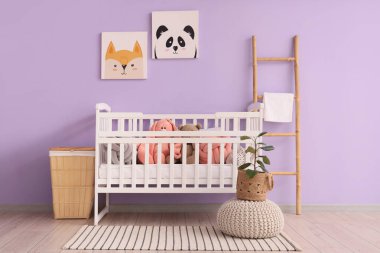 Bebek karyolasında, merdivenli ve sepetli şirin oyuncaklar mor duvarın yanında.