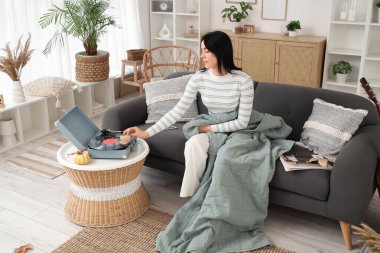 Sıcak ekoseli ve pikaplı genç mutlu kadın evdeki kanepede oturuyor.