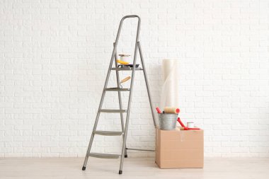 Beyaz tuğla duvarın yanında boyacı malzemesi olan merdiven.