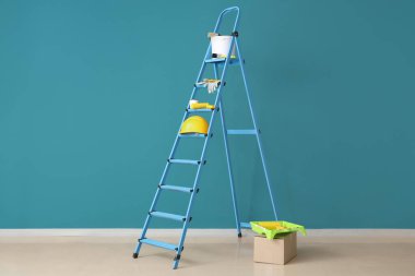 Mavi duvarın yanında boyacı malzemesi olan merdiven.