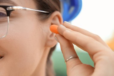 Female builder inserting earplugs outdoors, closeup clipart