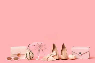 Şık çantaları, aksesuarları, şemsiyesi ve pembe arka planda balkabakları olan bej topuklu ayakkabılar.