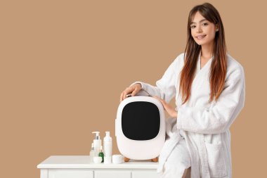 Bej arka planda kozmetik ürünleri için küçük buzdolabı olan güzel genç bir kadın.