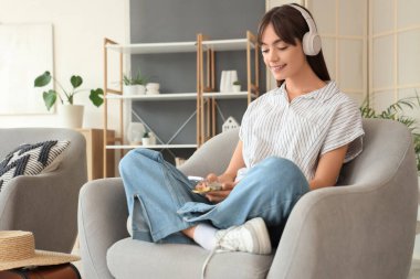 Kulaklıklı ve pusulalı bir bayan turist evdeki koltukta cep telefonu kullanıyor.