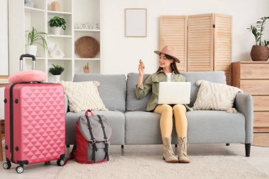 Evdeki kanepede dizüstü bilgisayar kullanan pusulası olan kadın turist.