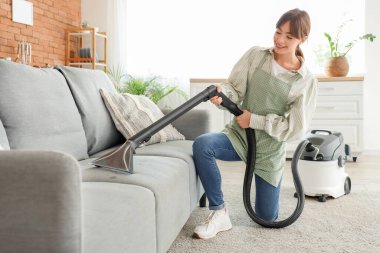 Evinde elektrikli süpürge kanepesi olan genç ve güzel bir kadın.