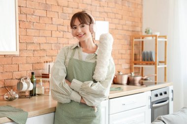 Mutfakta kulaklıkları ve tozluğu olan güzel bir kadın.