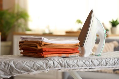 Ütü masasında demir ve çarşaf yığını, yakın çekim.