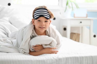 Pijamalı, tatlı, mutlu bir çocuk. Evde, yatağında maske takıyor.