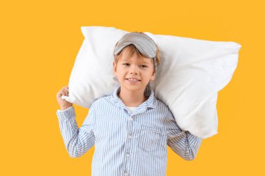 Sarı arka planda uyku maskesi ve yastığı olan pijamalı şirin, mutlu bir çocuk.