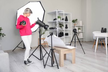 Stüdyoda çalışan profesyonel kamera ve ekipmanlı güzel genç bayan fotoğrafçı.