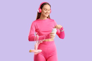 Kulaklık takmış genç bir kadın. Genişletici ile leylak arka planda su şişesi açıyor.