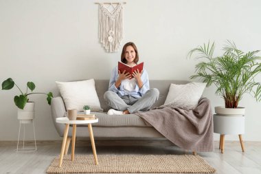 Evdeki kanepede kitap okuyan hayalperest genç kadın.