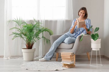 Evdeki koltukta kitap okuyan güzel genç bir kadın.